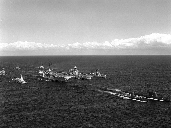 Seven ships follow two submarines in formation.